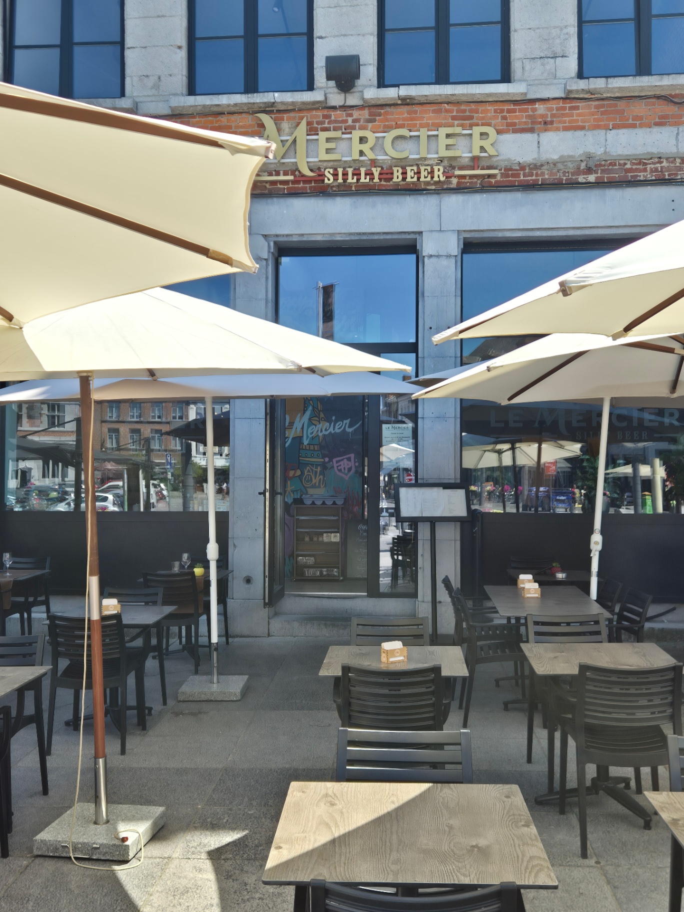 Enseigne dorée Le Mercier Silly Beer au-dessus de la terrasse et de ses parasols crème